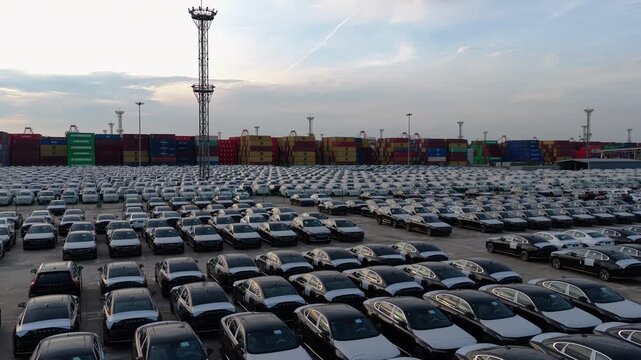 Car storage yard at seaport with container stacks and industrial tower at sunset