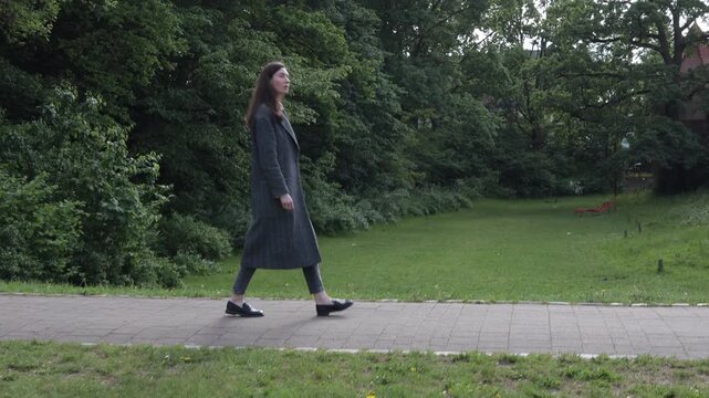 Woman in coat walking on paved path through green parkland