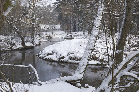 malerischer Flusslauf im verschneiten Winterwald mit umgest&uuml;rzten B&auml;umen