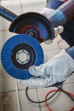 Worker holding a blue flap disc and an angle grinder, ready for metalworking