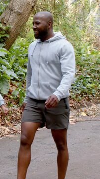 Vertical video: Starting stride man in hoodie, walking paved path, smiling, waving at offstage call