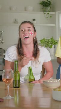 Vertical video: Smiling woman Eng cross holding green beer at home snacking as pal passing reacting
