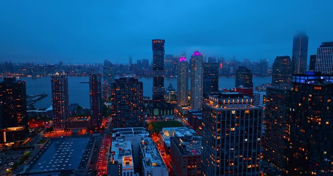 Jersey City high-rise buildings and Hudson River lights. Night aerial view of Jersey City towers, illuminated windows, streets, waterfront, and cloudy blue sky