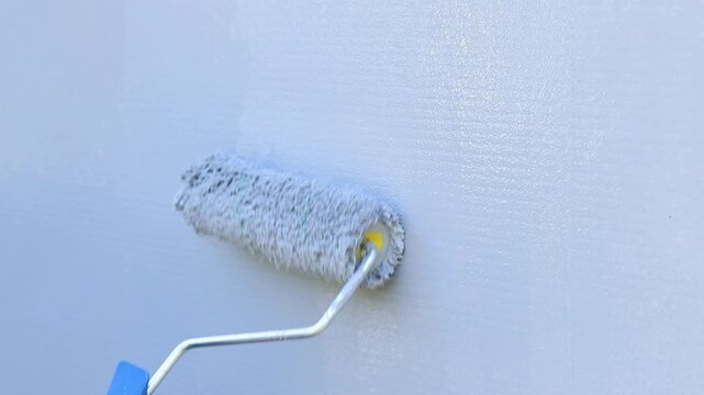Painting a wall with a roller in gray. The process of applying gray paint to the surface using a paint roller. The master's hand applies a layer of gray paint to the wall using a textured paint roller