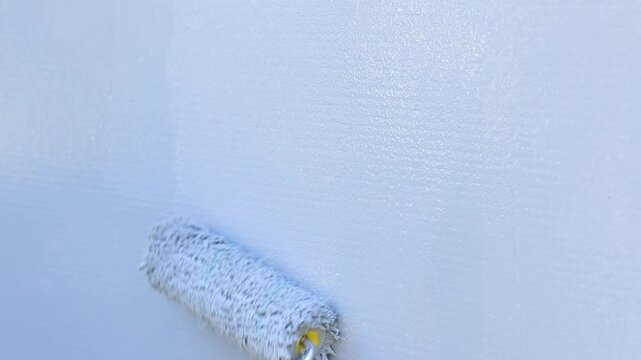 Painting a wall with a roller in gray. The process of applying gray paint to the surface using a paint roller. The master's hand applies a layer of gray paint to the wall using a textured paint roller