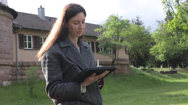 Woman using tablet outdoors near building and trees