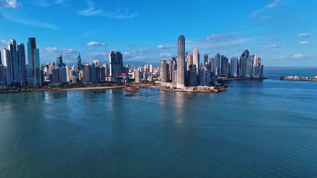 Punta Paitilla skyline across calm Panama Bay. Elevated view of Punta Paitilla towers, calm bay water, shoreline rocks, blue sky and daylight