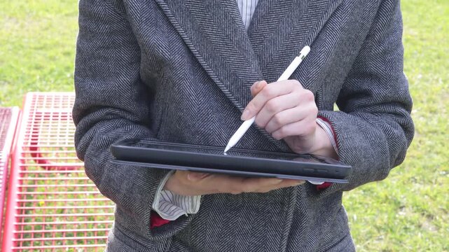 Person using a stylus on a tablet outdoors with a blurred background