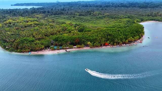 Caribbean beach shoreline with speedboat wake aerial view. Aerial view of palm-lined beach, turquoise water, anchored boats, speedboat wake and dense forest