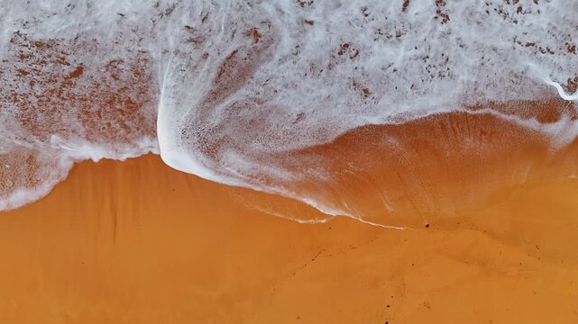 Top View of Panama Surf on Orange Sand. Top-down drone view of white ocean foam over orange Panama beach sand with shoreline patterns.