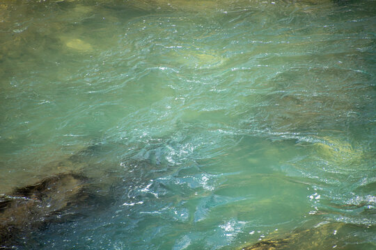 A detailed shot of the shimmering, turquoise surface of a mountain river in Spl&uuml;gen, Switzerland. The image captures the natural texture of flowing water and light reflections in the Alps.