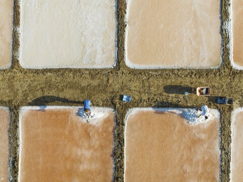 Harvesting salt at the saline ponds near Chiclana de la Frontera. The orange-red colour depends on the level of salinity and is directly caused by the algae Dunaliella salina and brine shrimp. Aerial view. Drone shot. C&aacute;diz province, Andalusia, Spain
