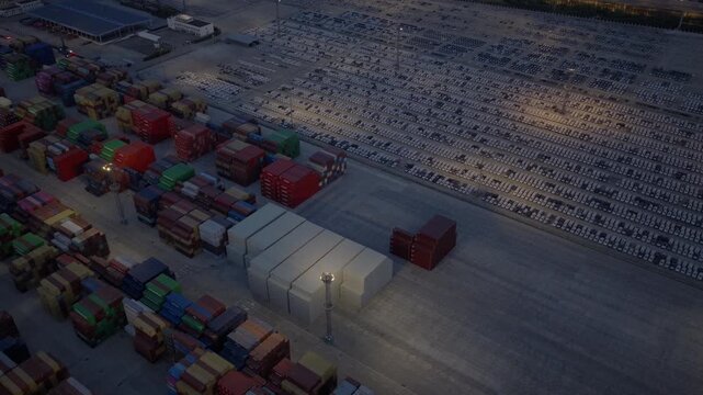 Aerial view of container stacks beside illuminated automobile yard at night