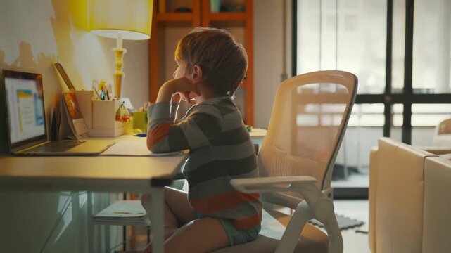 Child learning at desk with computer in a home setting during afternoon hours
