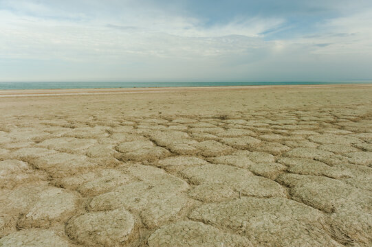 Cracked dry earth and soil crust in the foreground with the shallow waters of the Aral Sea in the background, Kazakhstan.