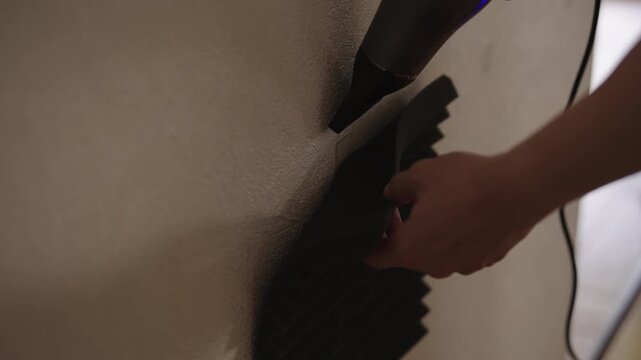 Close-up of professional hands applying heat with hair dryer to light brown leatherette material, removing creases and wrinkles from textured surface during repair or crafting process.