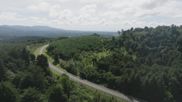 Aerial view of Lembus Forest featuring a winding asphalt road cutting through dense green canopy and rolling hills under a cloudy sky in Eldama Ravine, Baringo County, Kenya.