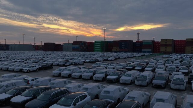 Sunset over rows of export cars and shipping containers at seaport terminal