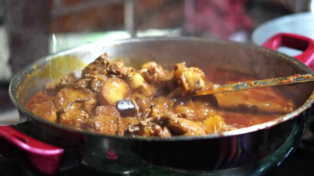 Traditional Indian Chicken Curry Cooking in Pan Close Up Spicy Food Video. Authentic Bengali style chicken curry with potatoes cooking in a steel pan with thick spicy gravy. Indian kitchen view.