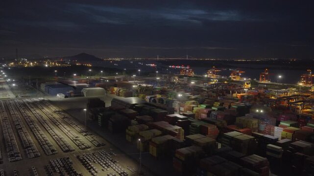 Wide night aerial view of car export yard and container terminal at industrial port