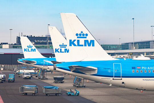 Amsterdam, Netherlands - 22.01.2026: Row of KLM Royal Dutch Airlines tails at the terminal gate with baggage carts and Schiphol sign in Amsterdam