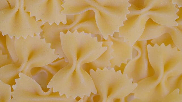 Uncooked pasta closeup. Farfalle pasta with soft shadows. Studio shot of pale yellow unfried farfalle. Detailed image of ricecolored bow tie pasta with ruffled edges