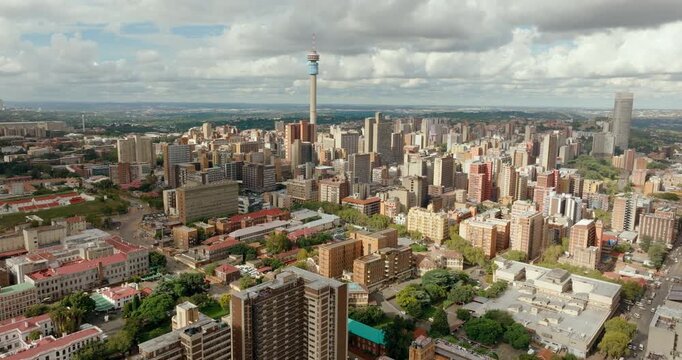 4K aerial tilt down shot starting from the Johannesburg skyline to the Hillbrow Tower. Dramatic drone movement capturing the dense urban architecture and South African city landscape
