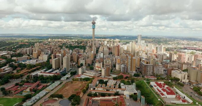 Aerial zoom in shot focusing on the Hillbrow Tower in Johannesburg, South Africa. High-angle 4K drone footage capturing the iconic telecommunications landmark and dense urban city architecture.