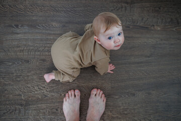 Naklejka premium Infant on all fours on a dark wooden floor looking up at a person standing nearby