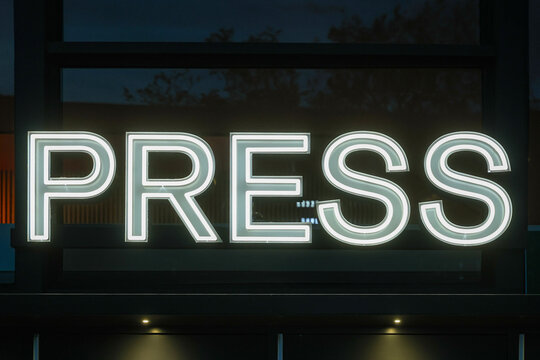 A neon sign with the word PRESS informs journalists where to enter the building for media coverage. 