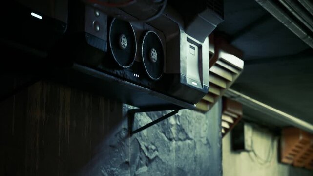 Black and silver tech equipment is mounted on a wall in a dimly lit indoor space. The design features circular speakers and a sleek amplifier, creating a modern aesthetic.