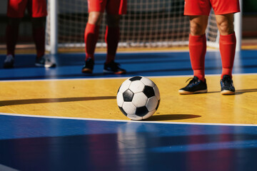 Fototapeta premium Futsal players stand on indoor court near goal. Soccer ball rests on yellow and blue surface. Sports competition warm up in sports arena. Active game awaits.