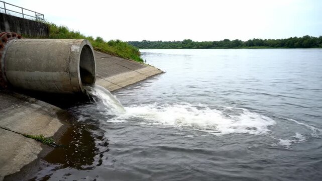 Concrete pipe discharging water into a river, with vegetation and trees in the background