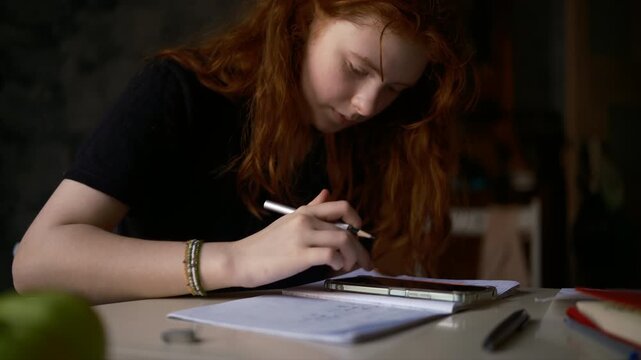 A teenage girl with red hair sits at home doing mathematics homework and preparing for exams. Cinematic video.