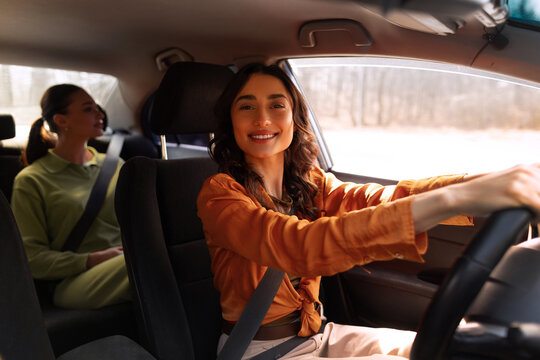 Happy woman driving car with female passenger sitting in back seat