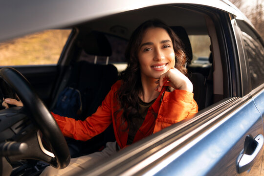 Happy young woman leaning on open car window with chin on hand