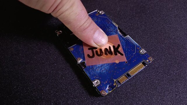 Hand sticking a junk written orange note onto damaged hard drive. Concept of AI synthetic data generation, corrupted data, e-waste recycling, system failure, broken and outdated equipment.