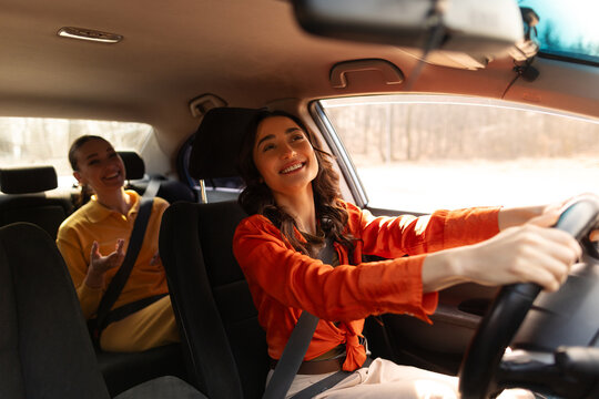 Two happy young women laughing together in car, driver smiling with passenger