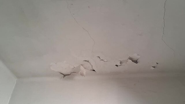 Damaged white ceiling showing deep cracks and peeling paint around an old circular light fixture
