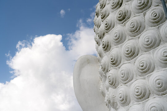 White Buddha head from behind against blue sky amd white clouds, Kandy, Sri Lanka