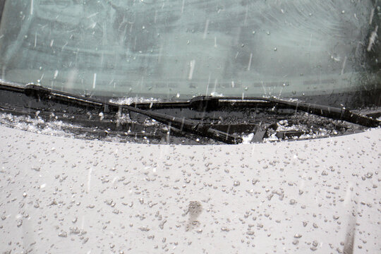 Hail stones falling on a silver car hood during a hailstorm