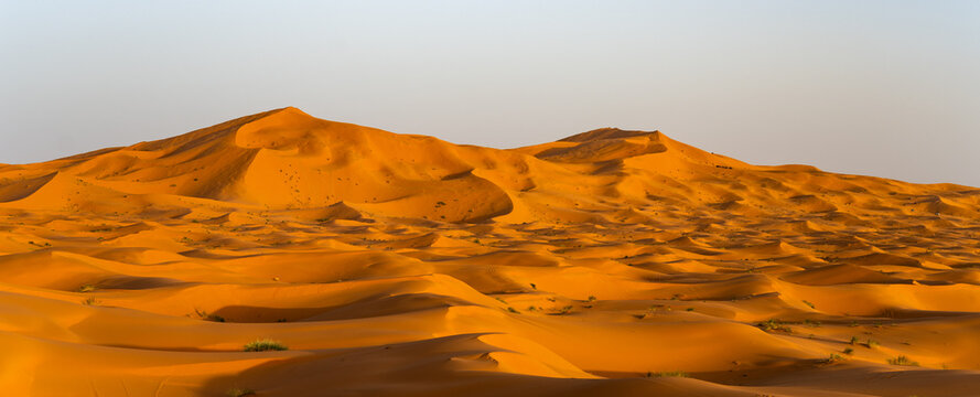 Waves of sand stretch across the horizon in Erg Chebbi near Merzouga, creating a look of natural patterns. The scene shows the beauty of the Sahara Desert during daylight.