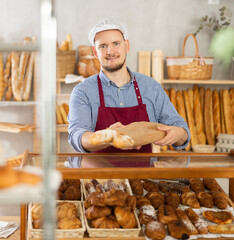 Obraz na płótnie Canvas Polite bakery worker places fresh baguette in paper bag