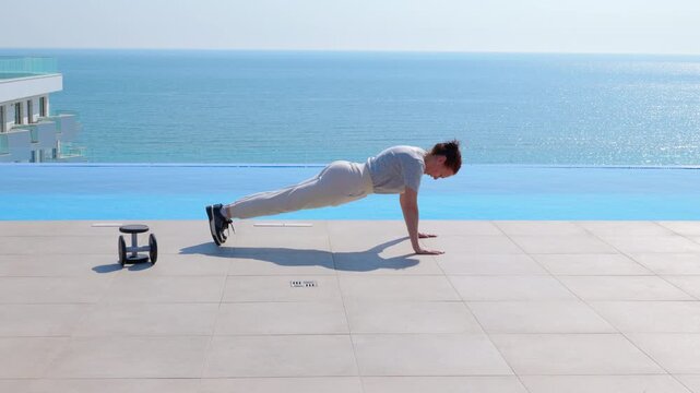 Athletic woman doing push-ups workout at an infinity pool. Athletic woman doing a strength training exercise by the infinity pool with a beautiful sea view in the background