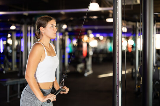 Slender athletic girl work out muscles of hands and arms on cable crossover machine in fitness club. Gym visitor trains tris, during classes at multi-station in wellness center.