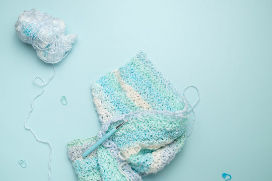 Blue and white crochet project laying on a blue surface with tools and supplies scattered about.