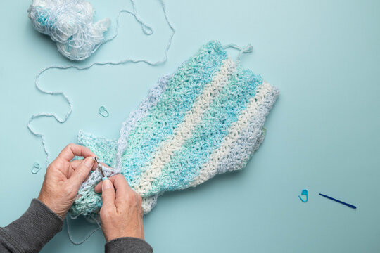 Elderly woman's hands, holds a crocheting project and crochet hook in her hands.