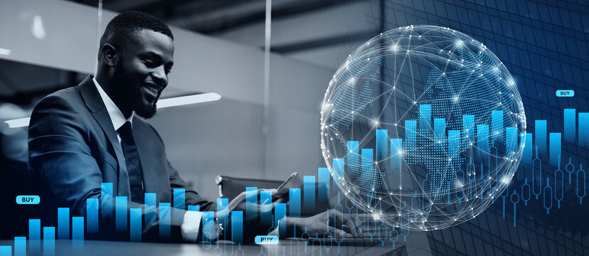 Handsome young black businessman in nice suit sitting at workdesk at modern office, using modern gadgets in business process, typing on laptop keyboard and holding smartphone, copy space