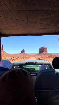 Point of view shot from a safari jeep with tourists driving on a dusty road towards the iconic mittens and buttes of monument valley, a popular destination on the arizona utah border