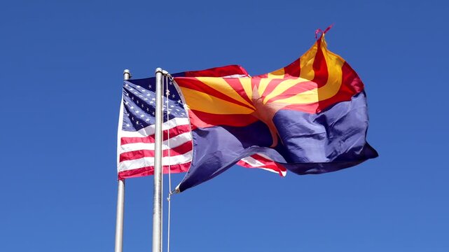 Majestic view of the arizona state flag and the united states flag flying side by side against a clear blue sky, symbolizing patriotism and state pride in a famous american landscape